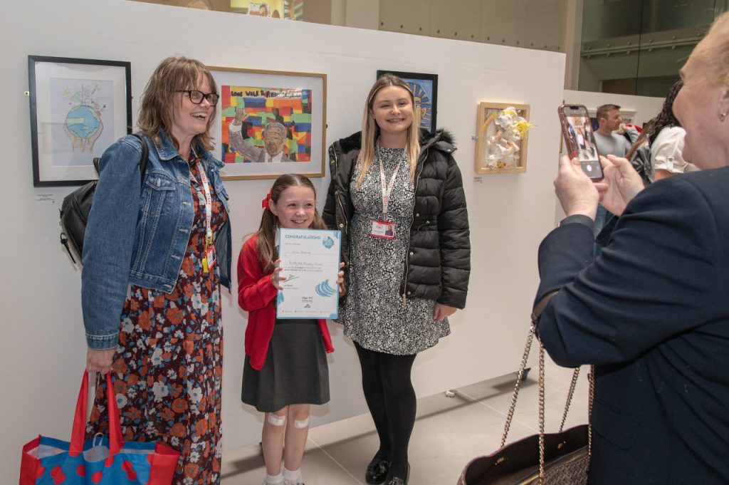 Child smiles with certificate from dot-art Schools competition