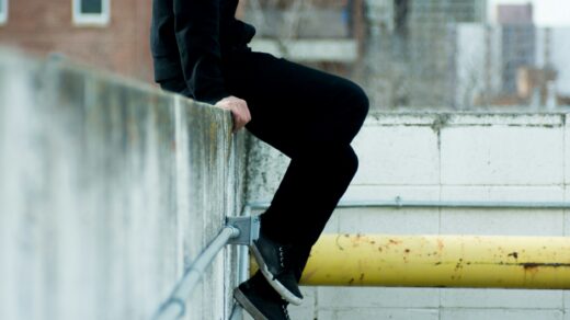Person sitting on white concrete wall near yellow metal pipe