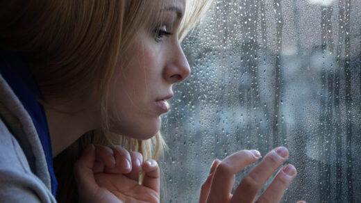 Sad young person looking out of window on rainy day