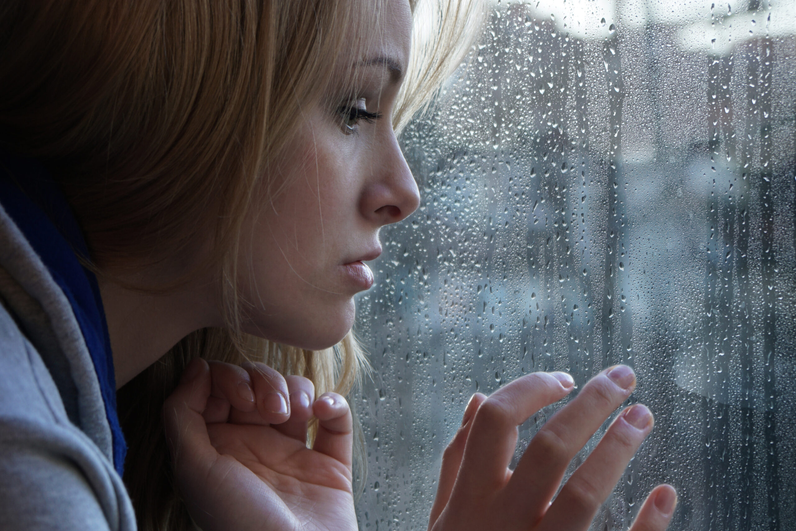 Sad young person looking out of window on rainy day