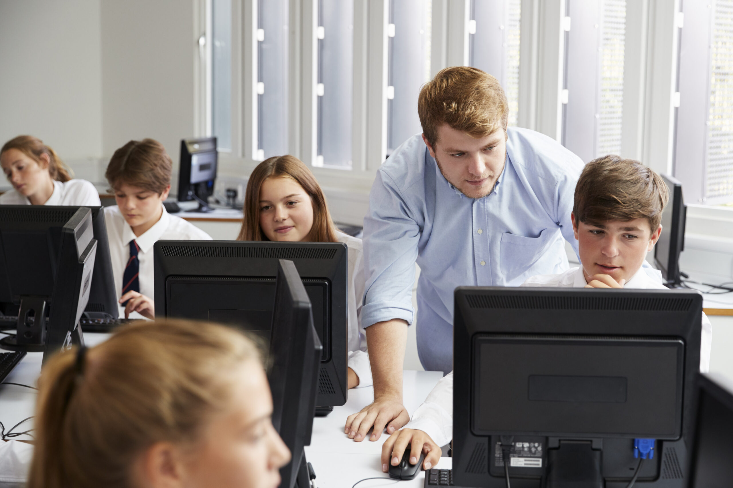 Students in uniform on computers while teacher observes